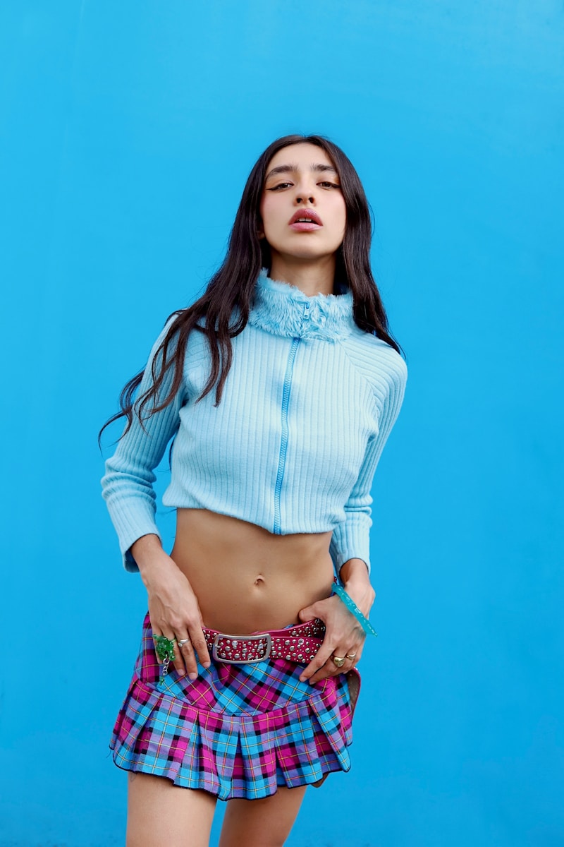 Woman in blue sweater and plaid skirt against blue wall