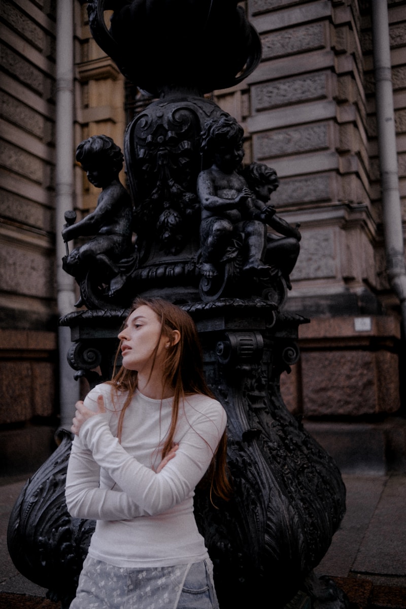 Woman in white shirt leans against ornate lamp post.