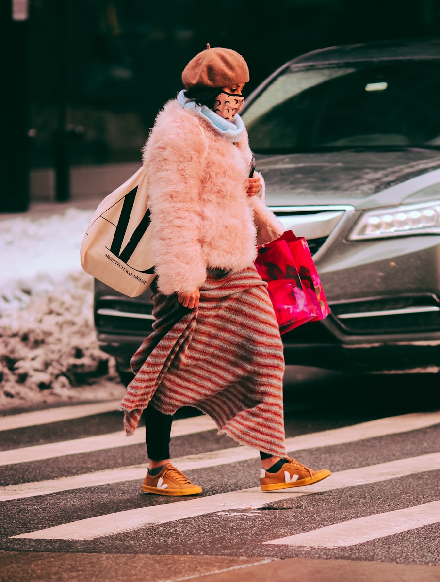 woman in white fur coat and red and black striped skirt standing on road during daytime